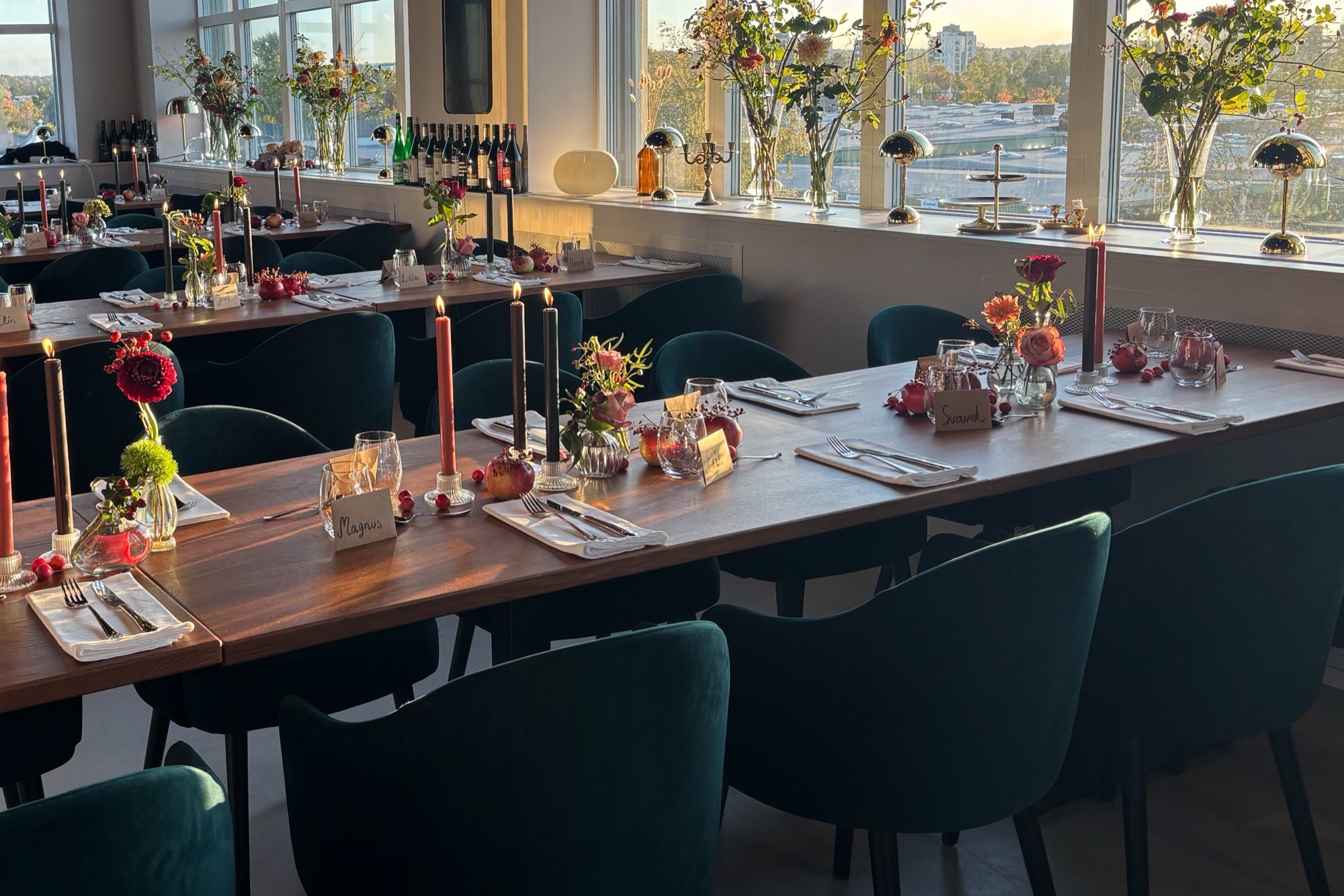 Restaurangen dukad för sällskap: tre långbord med levande ljus och blommor i kvällssol